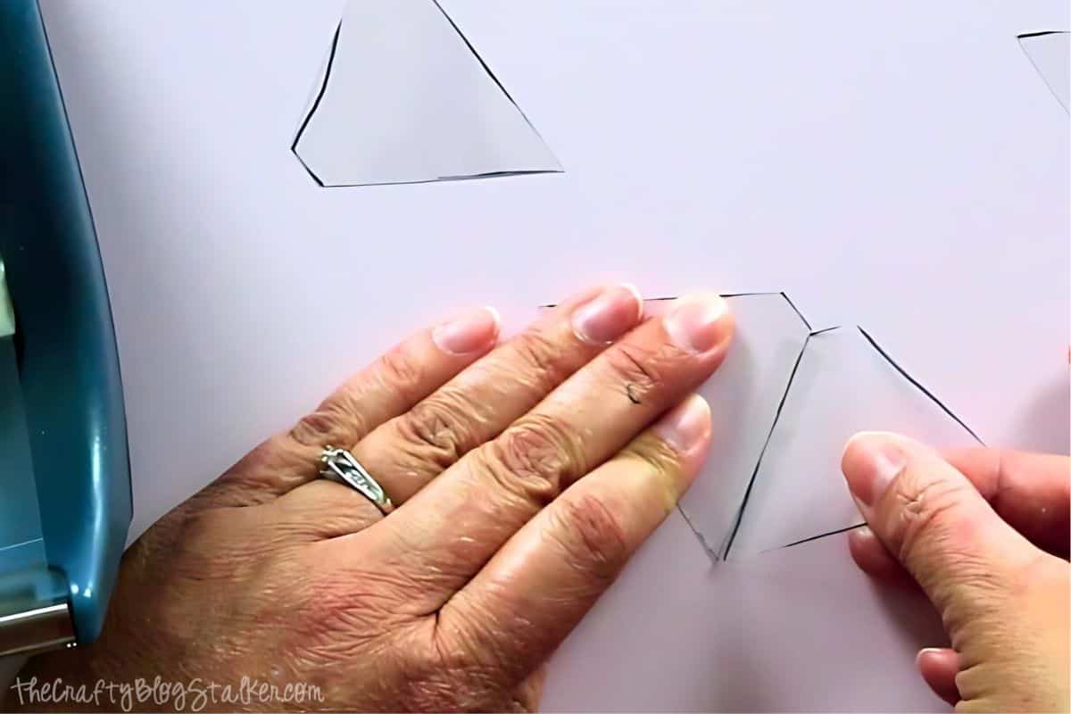 Hands assembling cut plastic pieces by taping the edges together to form a hologram projector, with clear plastic shapes outlined in black marker.