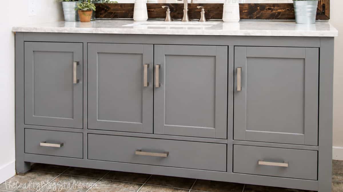 Gray bathroom vanity with shaker-style cabinet doors, silver hardware, and a white countertop in a modern bathroom.