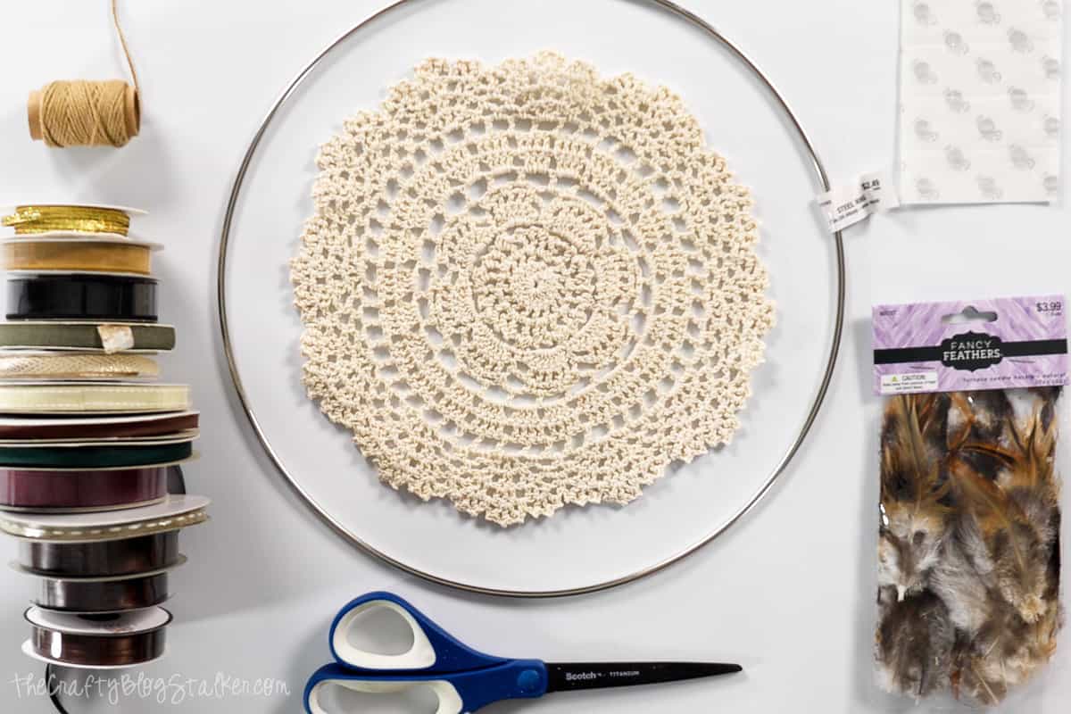 steel hoop, crocheted lace doily, twine, ribbon rolls, feathers, scissors, and glue dots