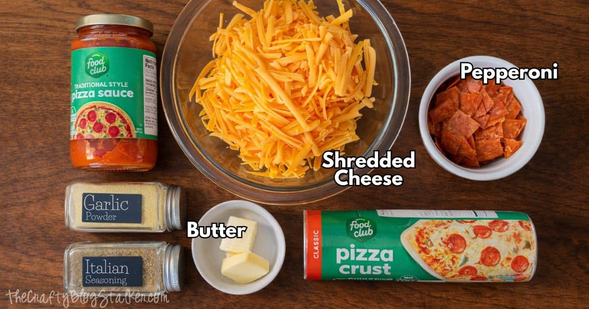 Ingredients for pizza roll ups including pizza sauce, shredded cheese, pepperoni, pizza crust, butter, garlic powder, and Italian seasoning on a table.
