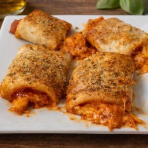 Close-up of baked pizza roll ups filled with sauce and melted cheese, topped with seasoning on a white plate.