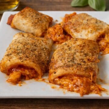 Close-up of baked pizza roll ups filled with sauce and melted cheese, topped with seasoning on a white plate.
