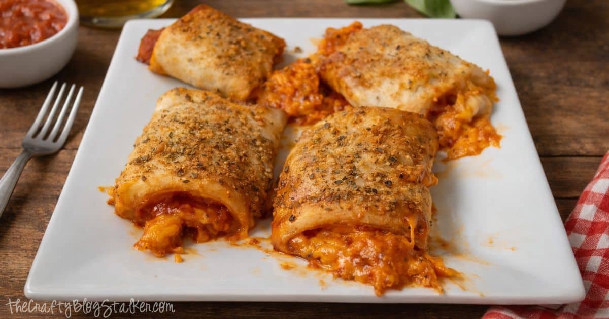 Plate of baked pizza roll ups filled with sauce and melted cheese, topped with seasoning and served with marinara on the side.
