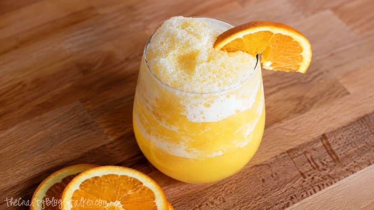 Homemade orange juice slushie in a glass topped with frothy ice and garnished with a fresh orange slice.