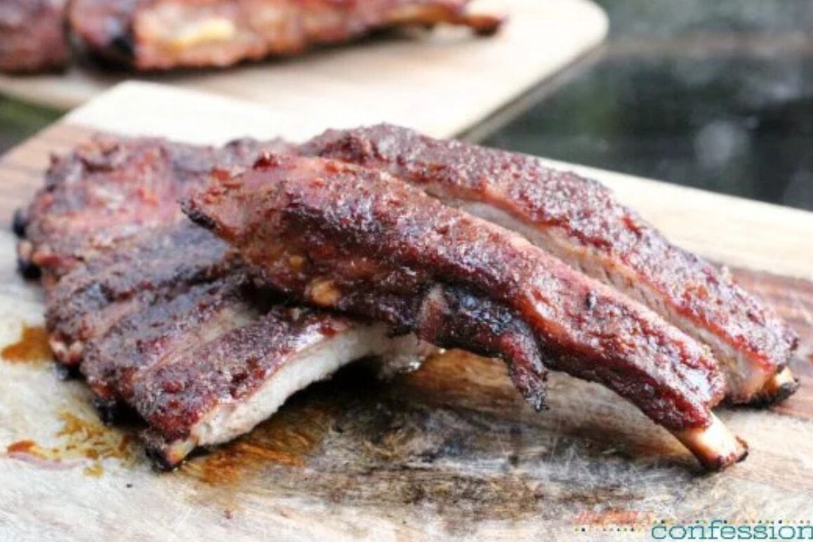 Close-up of juicy grilled pork ribs stacked on a wooden cutting board, showing a dark, caramelized crust and tender, smoky texture.