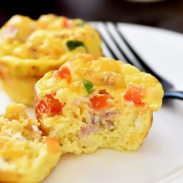 Mini egg muffin filled with diced ham, peppers, and green onions, shown cut open on a plate to reveal the soft, fluffy baked egg interior.