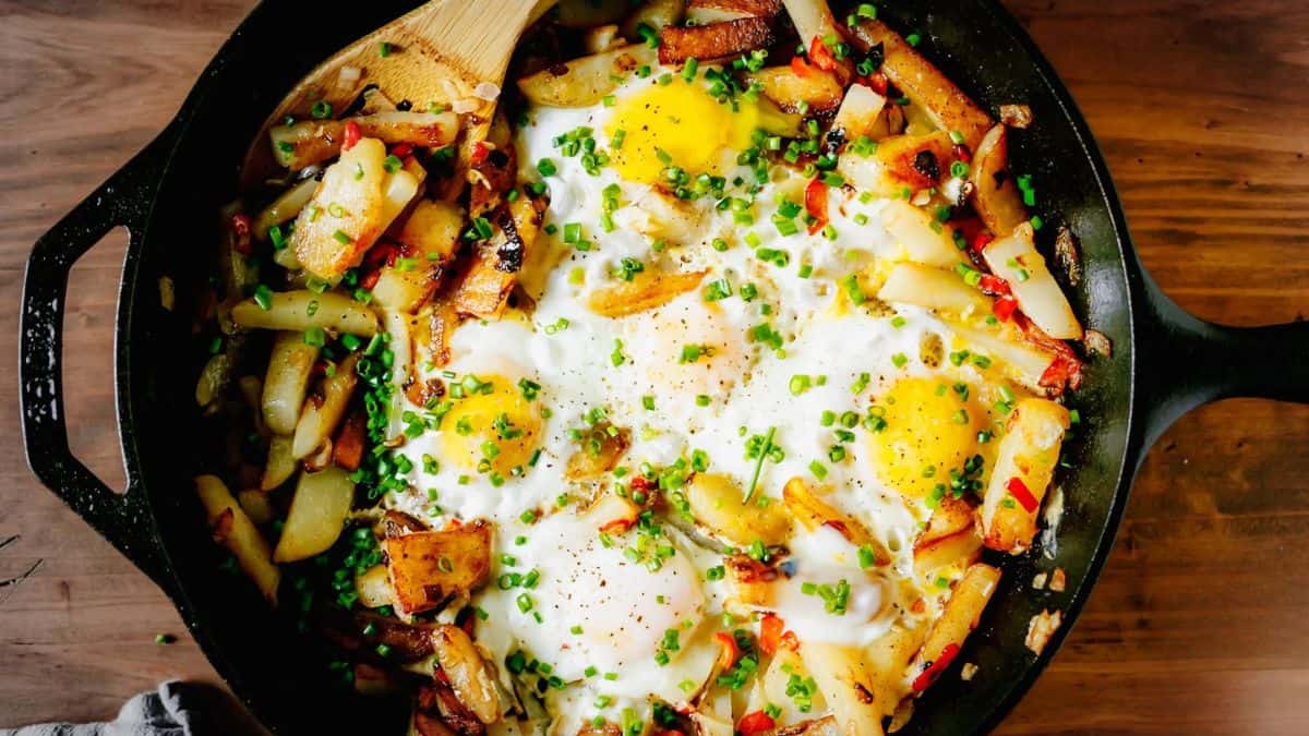 A cast-iron skillet filled with cooked potatoes, peppers, and onions topped with sunny-side-up eggs and chopped chives.