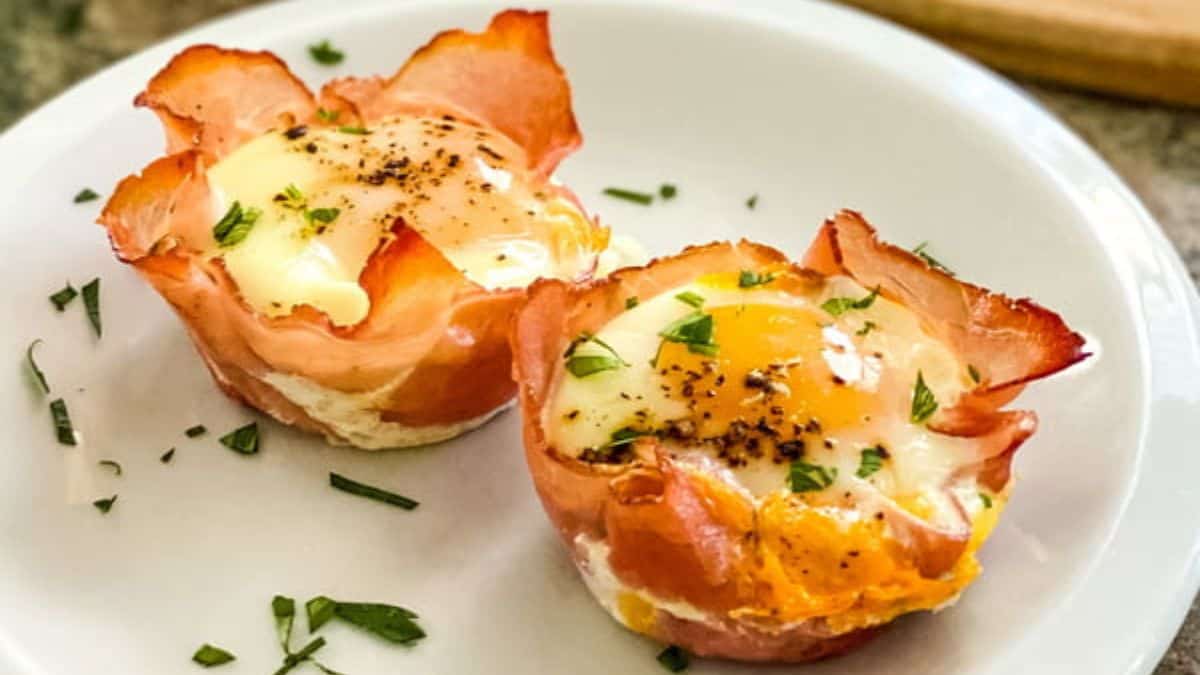 Two baked ham and egg cups topped with herbs, served on a white plate.