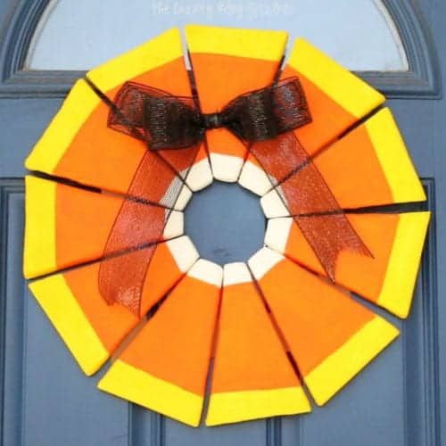 the finished candy corn wreath hanging on a blue door