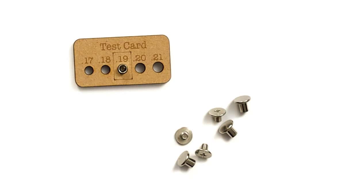 MDF test card labeled with hole sizes 17-21, used to check screw fit. Several small silver Chicago screws are placed beside the card.