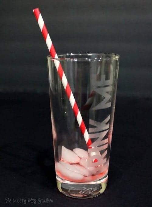 an empty "drink me" etched glass with a red striped straw