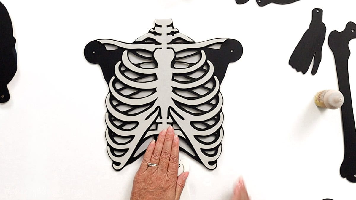 Hand gluing layered black and white laser cut ribcage pieces together to form part of a posable skeleton craft project.