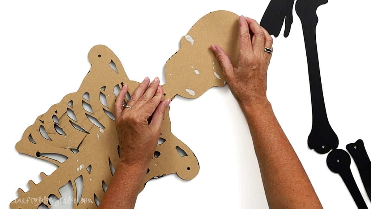 Hands attaching the back of a laser cut skull piece to the ribcage section of a skeleton craft, preparing to assemble the full posable skeleton.