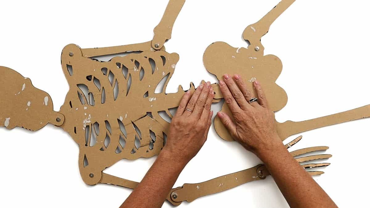 Hands connecting the top and bottom sections of a posable skeleton, attaching the ribcage to the hip with screws while other assembled limbs are visible.