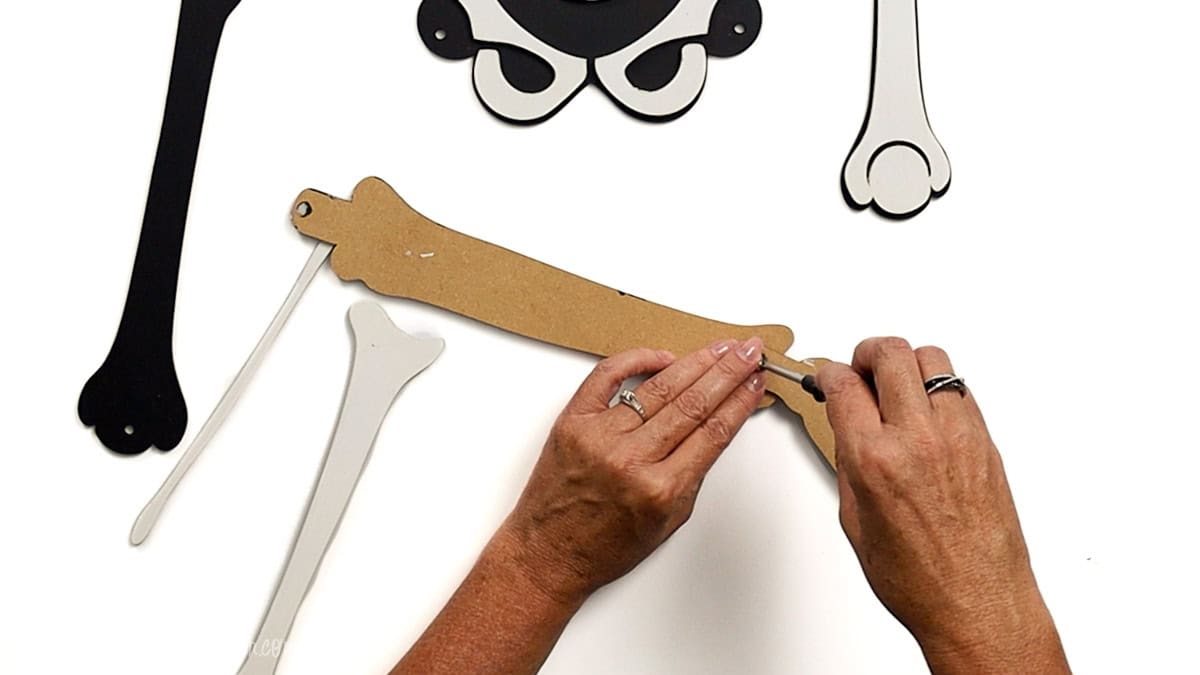 Hands attaching a joint to a laser cut skeleton leg using a screw casing, securing the ankle piece to the lower leg with other skeleton parts nearby.