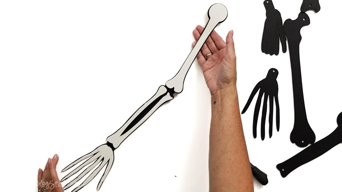 Hands holding a fully assembled laser cut skeleton arm with painted black and white bones, connected with screw posts for movable joints.