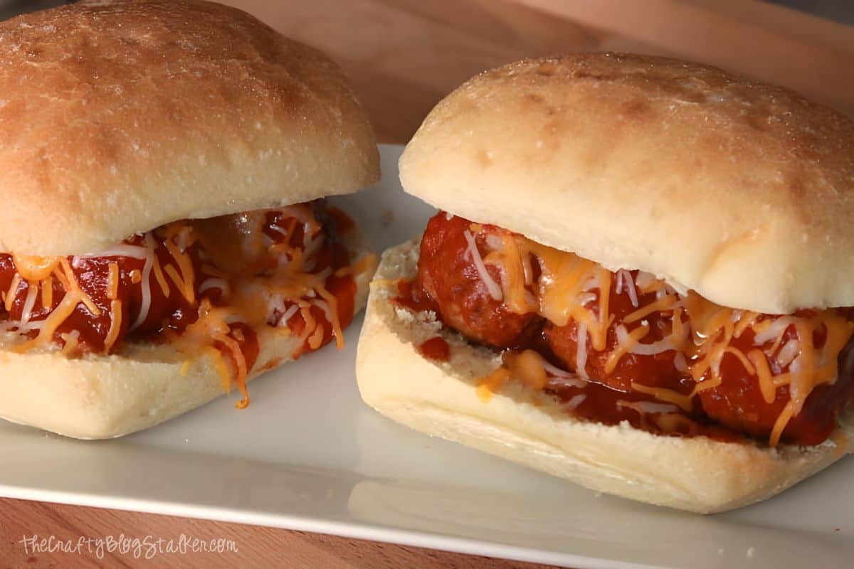 Two Meatball sandwiches on a white plate.