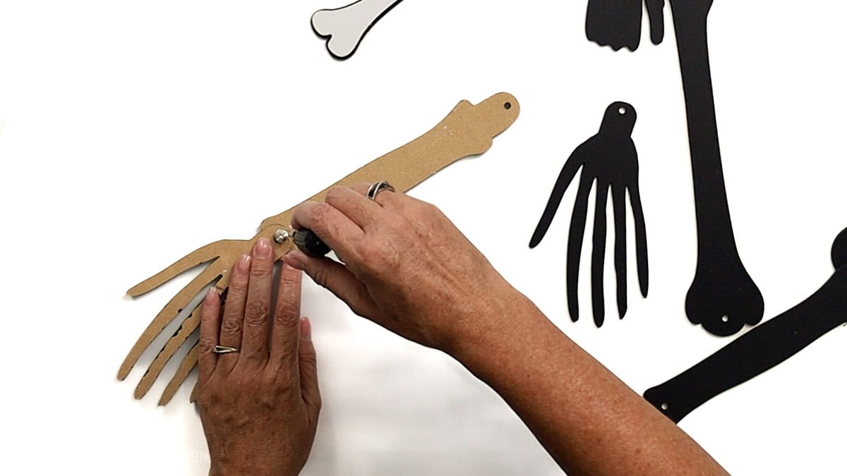 Hands attaching a screw post to connect a laser cut skeleton hand to a forearm piece, with additional black skeleton parts visible on the side.