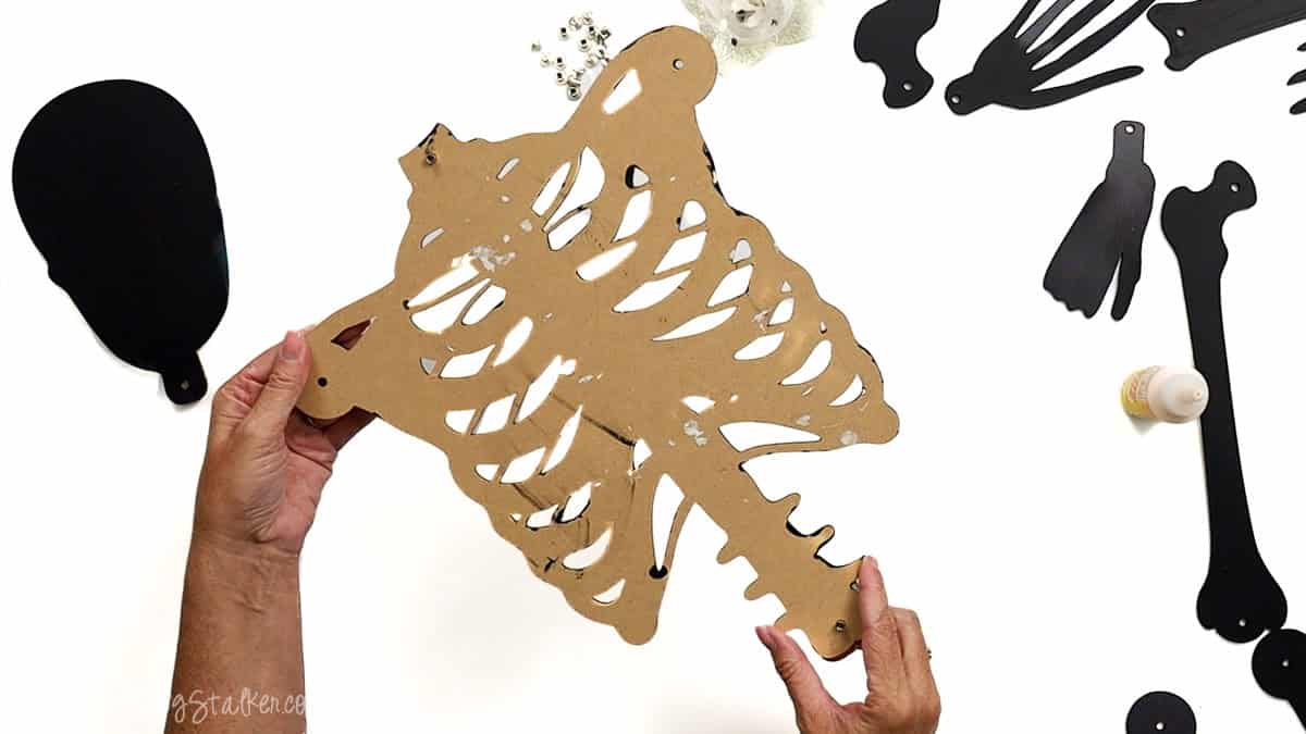 Hands holding the back view of a layered laser cut ribcage piece, showing glued edges and screw holes for assembling a posable skeleton craft.