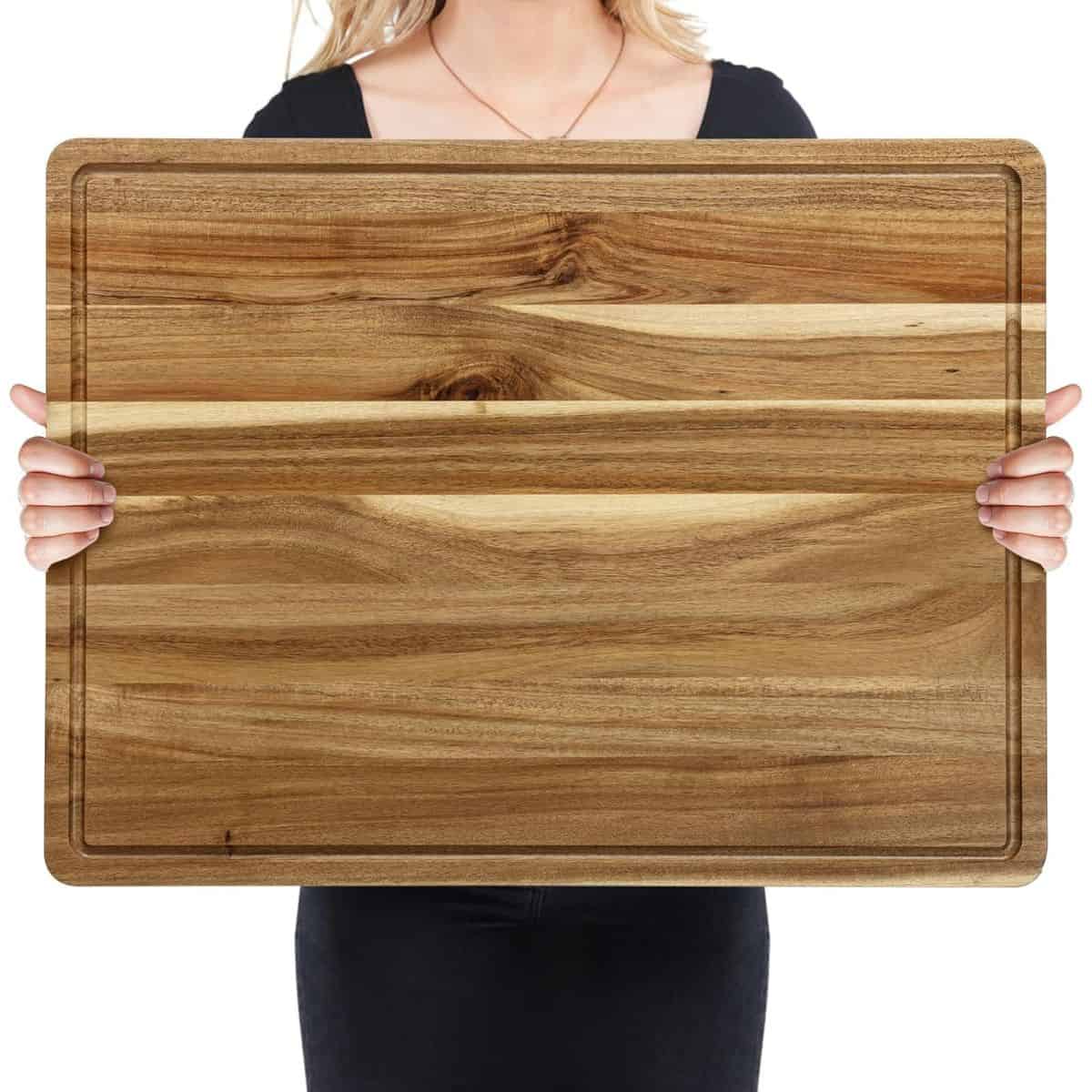 A person holding a large rectangular wooden cutting board with a juice groove, showcasing its smooth grain and natural wood finish.