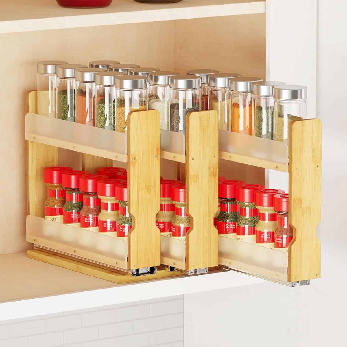 A bamboo pull-out spice rack neatly organized with glass spice jars and red-labeled seasoning bottles in a kitchen cabinet.