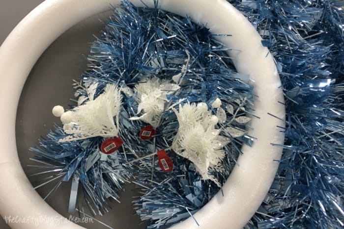 4 supplies used to make a winter wreath; blue garland, 3 white floral picks, styrofoam wreath form and floral pins.