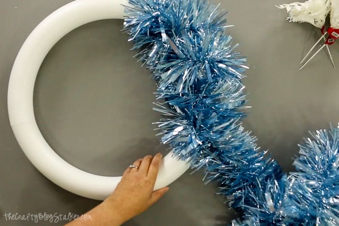 Wrapping a styrofoam wreath form with tinsel garland.