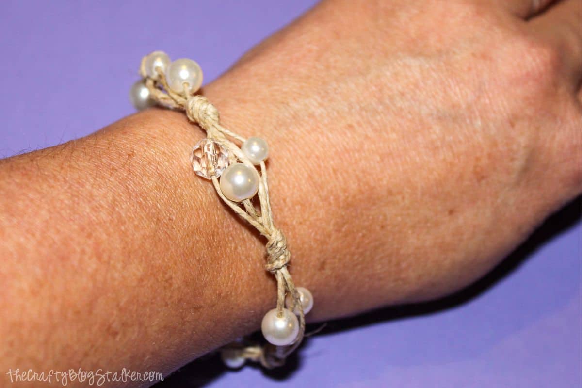 A twine and pearl bracelet on a wrist.