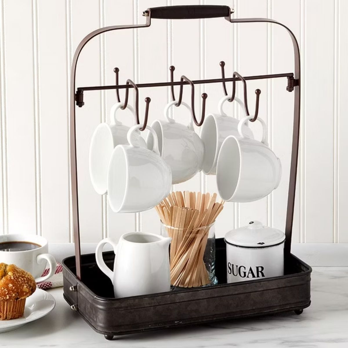 Countertop coffee mug rack holding hanging mugs, sugar canister, stir sticks, and a small pitcher, arranged as a coffee station organizer.
