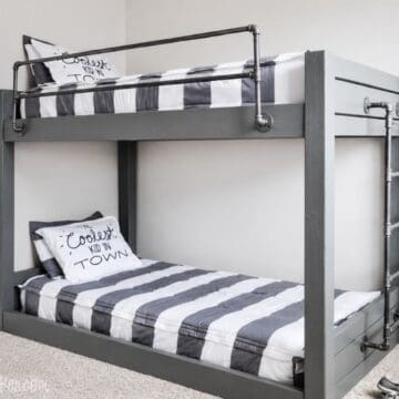 DIY industrial bunk bed with gray wood frame, metal pipe rails, ladder, and striped bedding in a modern bedroom.