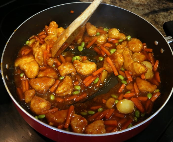 stirring orange chicken while it is cooking in a  pan on the stove 