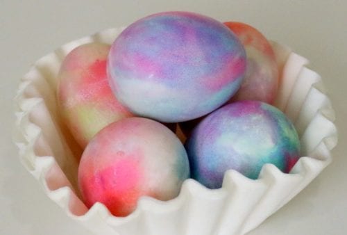 five hard boiled eggs that have been dyed in shaving cream and food coloring displayed in a white dish
