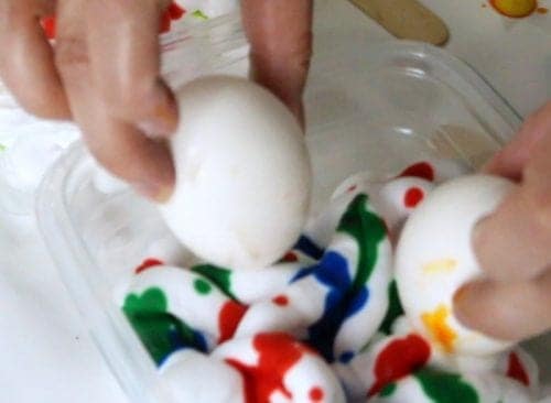 two hands dropping hard boiled eggs into shaving cream and food coloring mixture