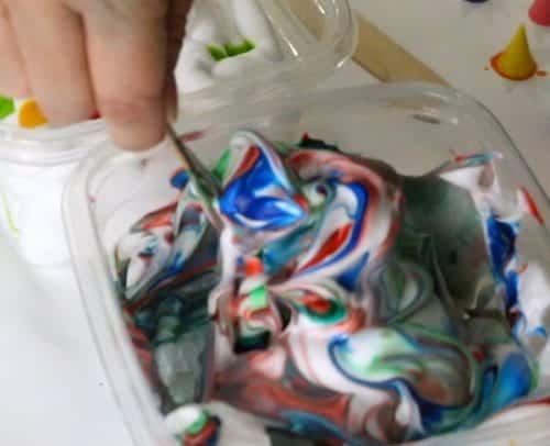 stiring eggs, shaving cream and food coloring with a wood stick