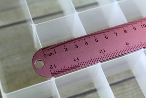 using a ruler to measure the compartment size in plastic organizer box