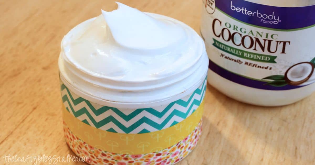 Jar of homemade body lotion with a smooth swirl on top, placed beside a container of coconut oil on a wooden surface.