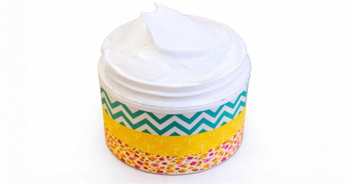 Small jar of white body lotion with decorative patterned labels around the container and a smooth swirl of lotion on top.