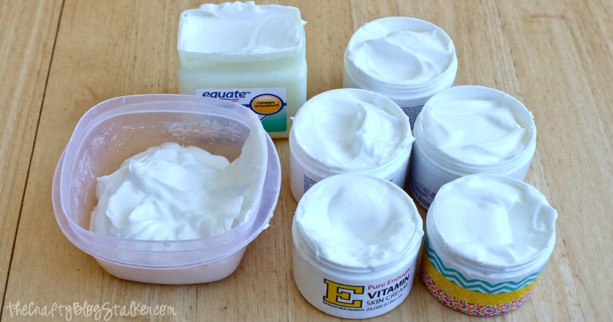 Multiple jars filled with homemade white lotion alongside a container of extra mixture, all set on a wooden surface.
