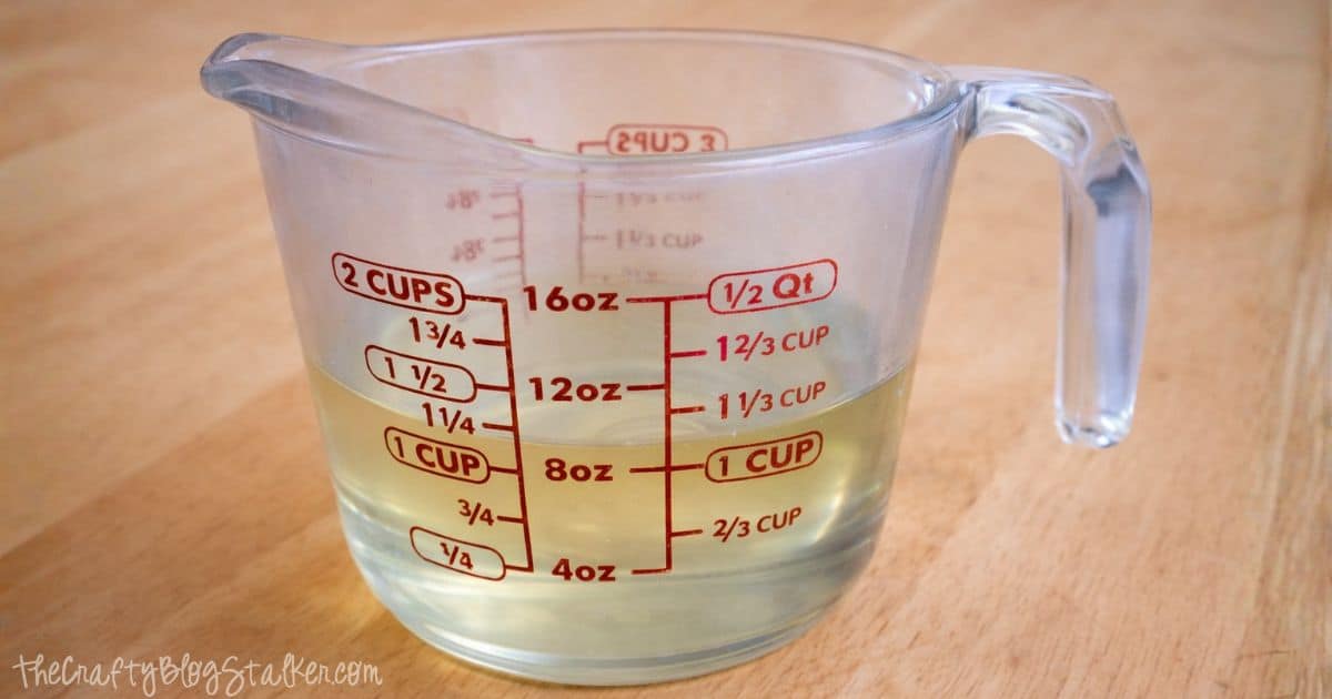 Glass measuring cup filled with melted coconut oil, showing measurement markings, placed on a wooden surface.