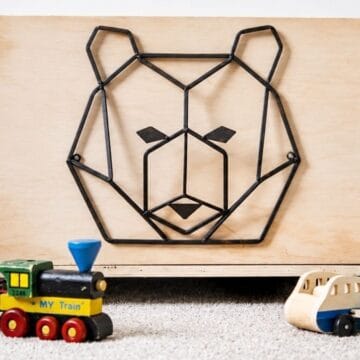Wooden rolling toy box with a geometric bear design on the front, displayed with toy trains and a wooden airplane on carpet.