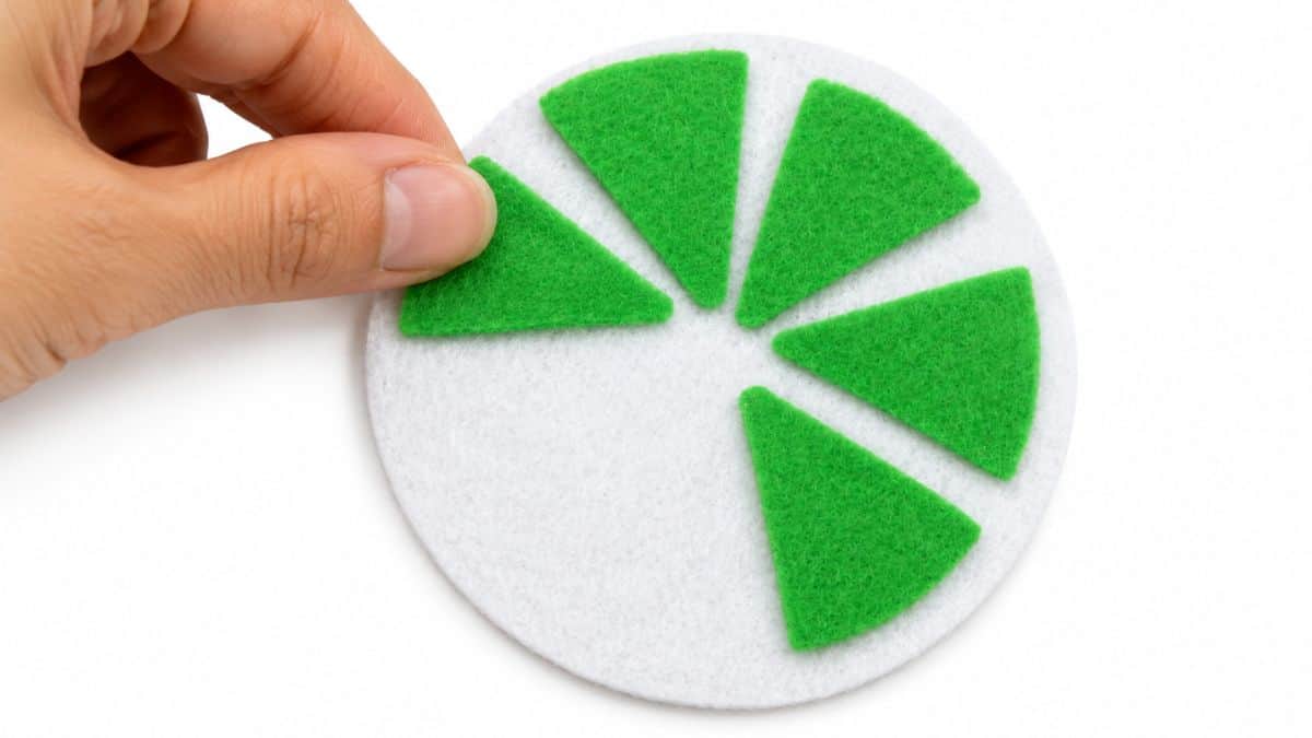 Hand placing green felt citrus segments onto a white felt circle while assembling a DIY lime slice coaster.