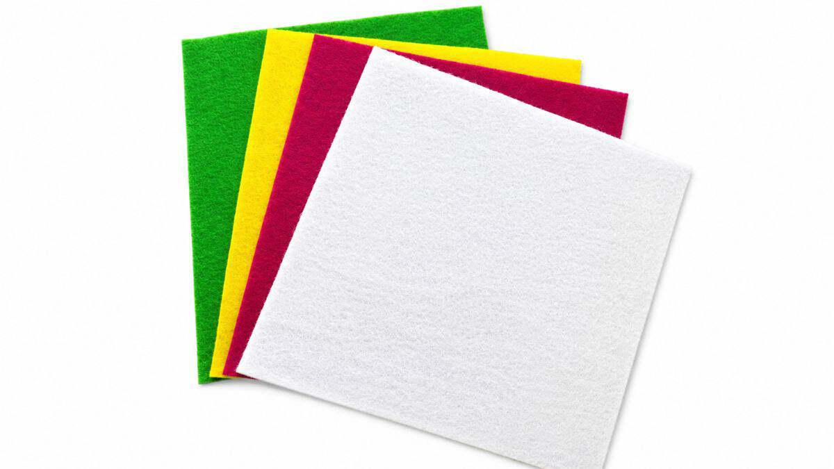 Stacked felt sheets in green, yellow, pink, and white arranged on a light gray background for a colorful craft project.