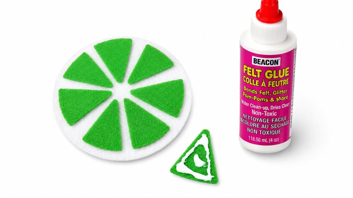 Felt lime slice coaster pieces arranged on a white felt base beside a bottle of felt glue and a glued green felt segment.
