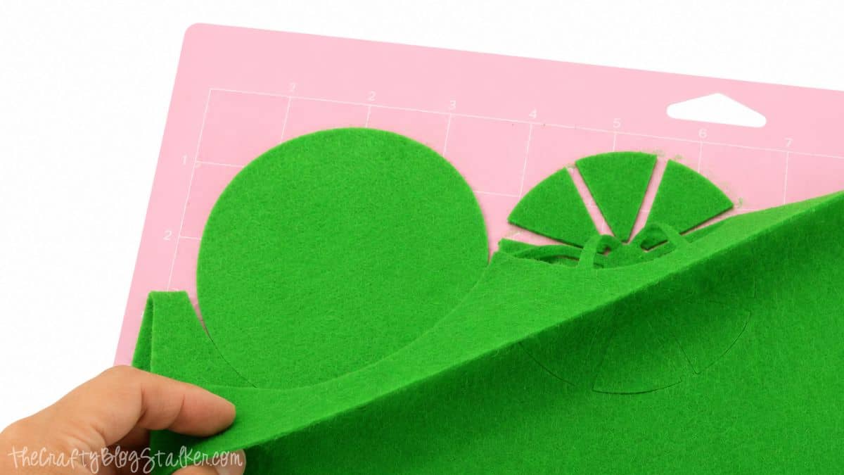 Hand removing green felt citrus coaster pieces from a pink Cricut cutting mat after cutting with a Cricut Maker machine.