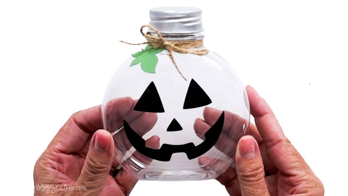 Clear pumpkin-shaped jar decorated with a black jack-o'-lantern face, green leaf, and twine bow, ready to fill with Halloween candy.