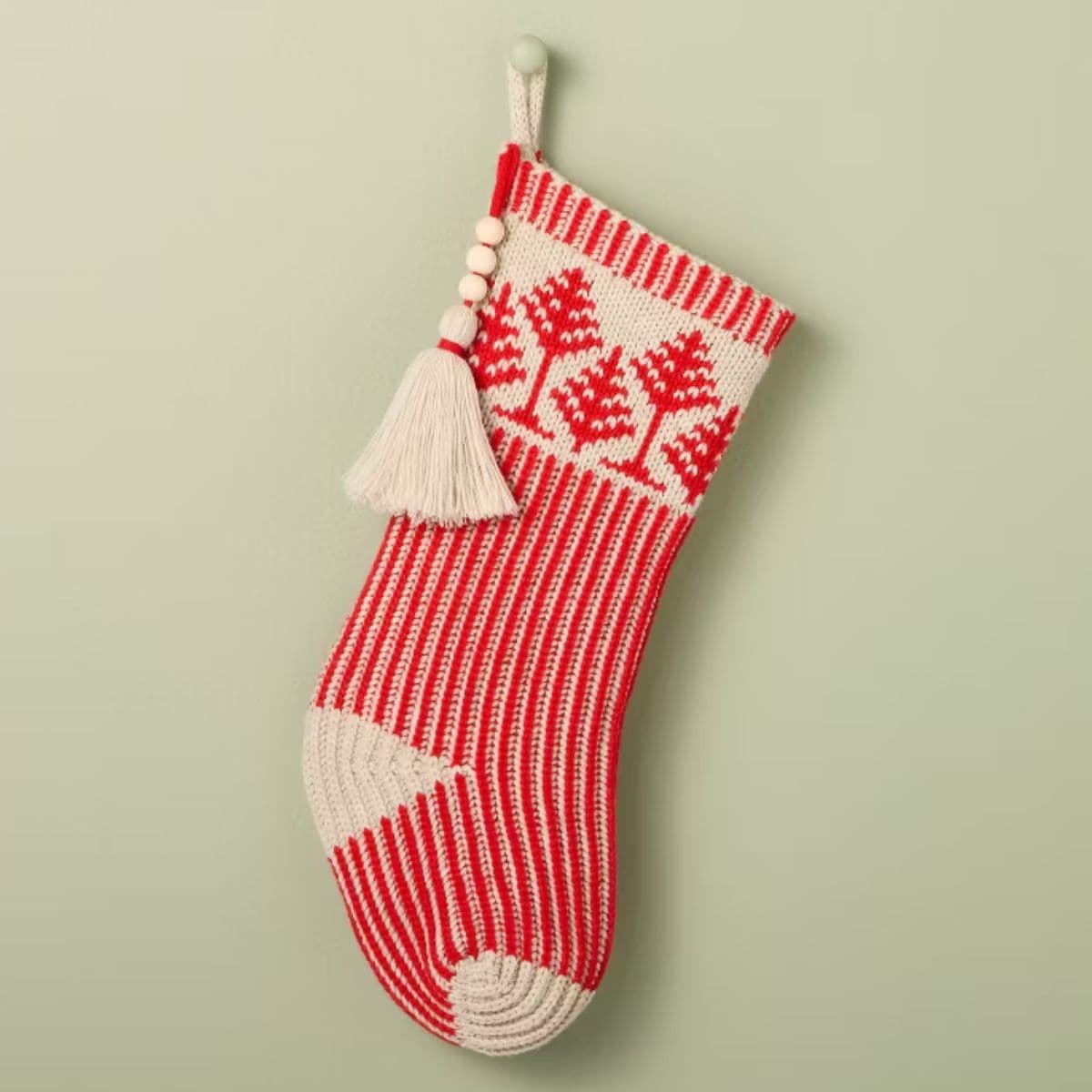 Red and cream knit Christmas stocking with tree patterns, vertical stripes, and a tassel with wooden beads hanging from the side.
