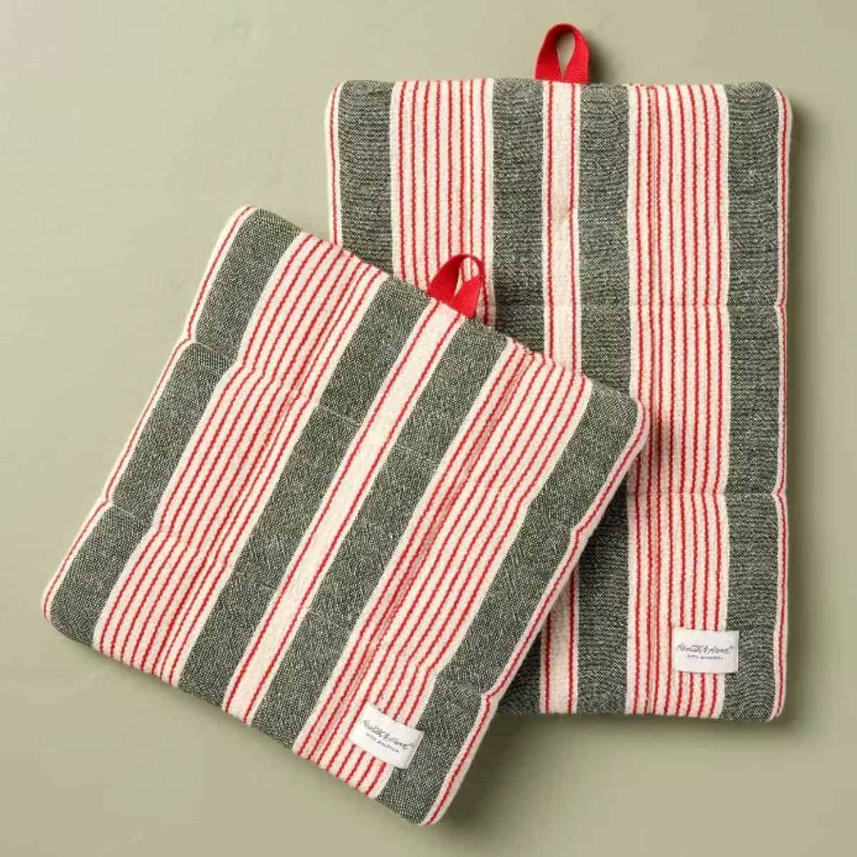 Set of two quilted Christmas potholders with red, white, and dark green stripes, red hanging loops, and fabric labels.