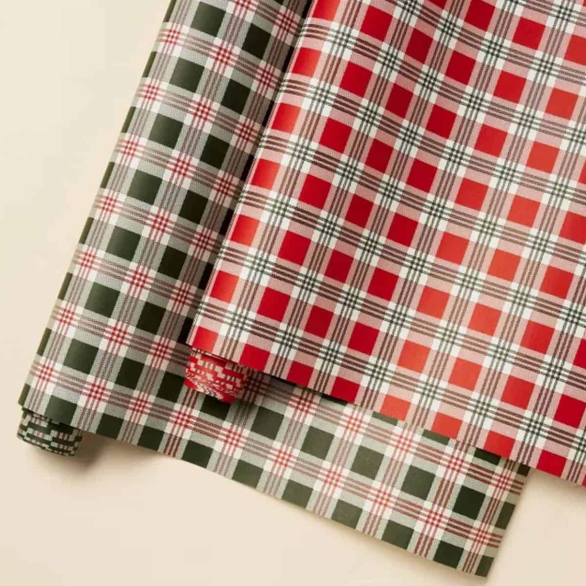Red and green plaid Christmas wrapping paper with overlapping sheets featuring classic holiday patterns on a cream background.
