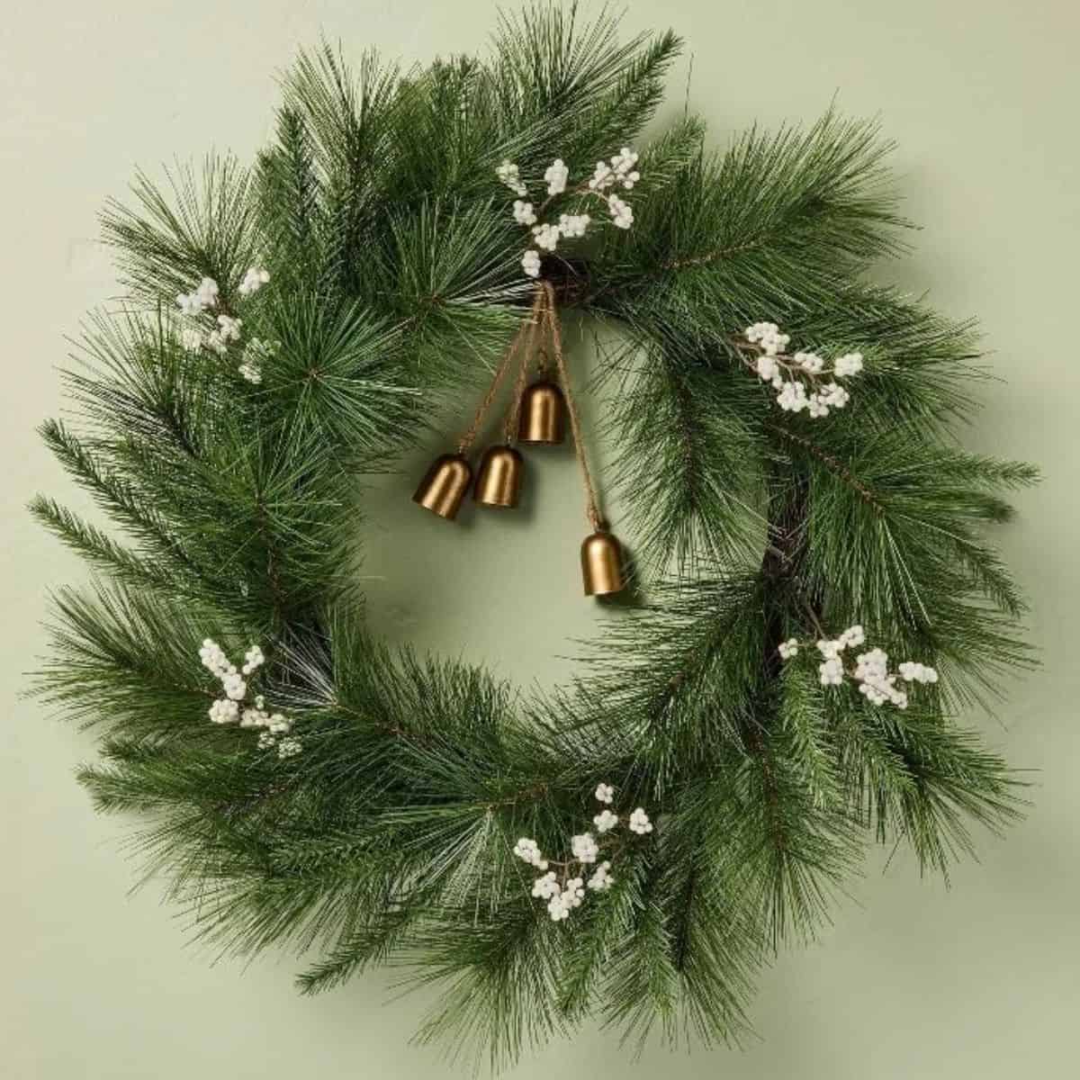 Long needle pine Christmas wreath decorated with white berry clusters and four gold bells hanging from rustic twine.