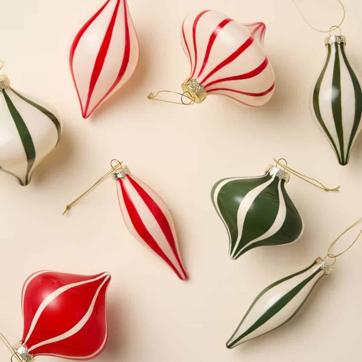Red, green, and white striped glass Christmas ornaments in twisted teardrop shapes with metallic caps and gold hanging strings.